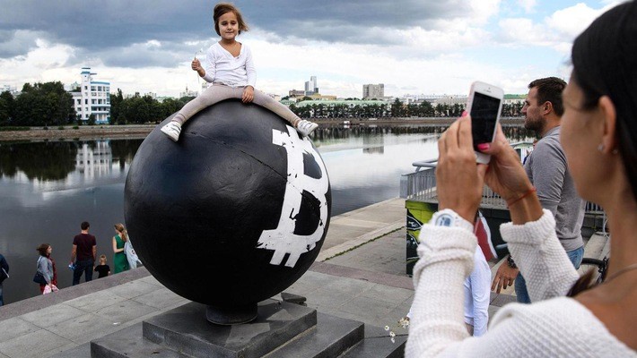 Bé gái tạo dáng để chụp ảnh trên một quả cầu có biểu tượng tiền ảo Bitcoin trên một quảng trường ở Yekaterinburg, Nga - Ảnh: Tass/Getty/CNBC.