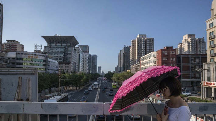 Một phụ nữ cầm ô đi dưới bầu trời trong xanh ở thủ đô Bắc Kinh của Trung Quốc, tháng 7/2018 - Ảnh: Bloomberg.