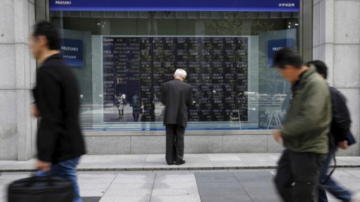 Một người đàn ông đứng xem bảng giá cổ phiếu trên đường phố ở Tokyo, Nhật Bản, tháng 4/2018 - Ảnh: Reuters.