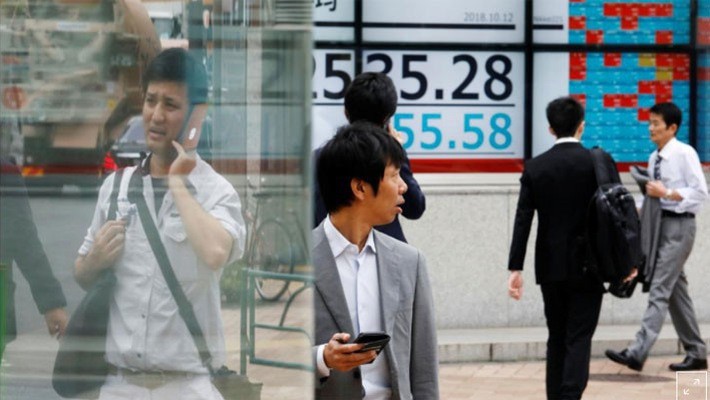 Những người bộ hành đi qua một bảng điện tử chứng khoán trên đường phố Tokyo hôm 12/10 - Ảnh: Reuters.