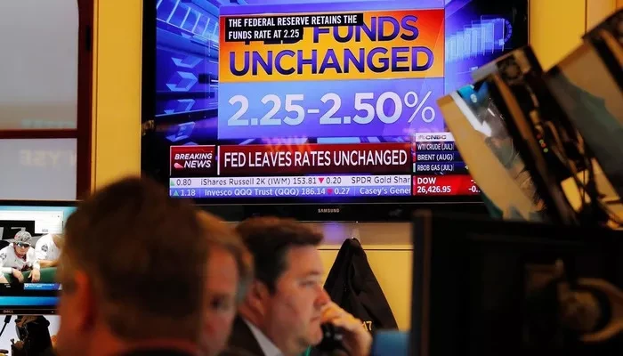 Các nhà giao dịch cổ phiếu trên sàn NYSE ở New York, Mỹ, ngày 19/6. Một màn hình trên sàn giao dịch đang phát sóng bản tin về việc FED giữ nguyên lãi suất - Ảnh: Reuters.