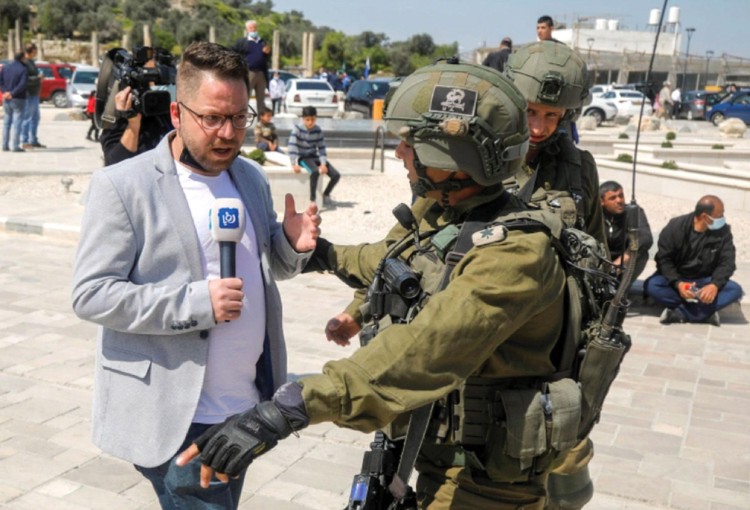 Một phóng viên truyền hình đối diện quân lính Israel tại khu vực Bờ Tây vào tháng 3/2021