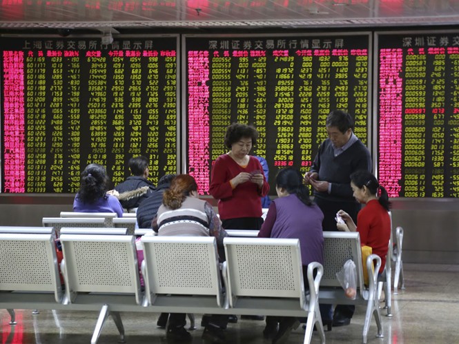 Các nhà đầu tư Trung Quốc chơi bài trước một bảng điện tử thể hiện các chỉ số chứng khoán ở Bắc Kinh - Ảnh: Reuters